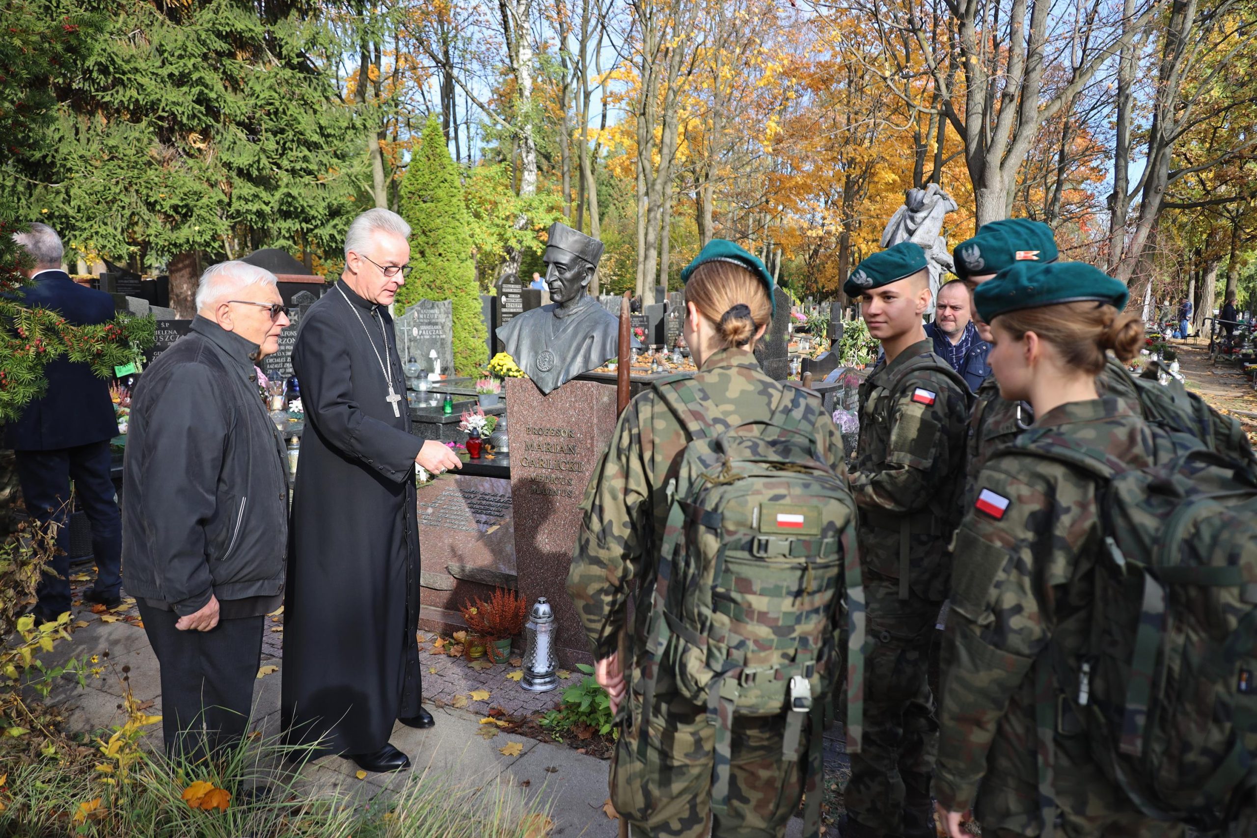 Żołnierze salutują zmarłym żołnierzom nad ich grobami, razem z nimi ksiądz.