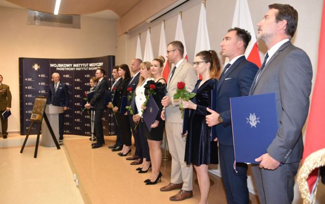 Rozpoczęcie roku akademickiego w wojskowym instytucie medycznym. Ceremonia rozdania dyplomów w auli. Studenci stoją na podeście przy ścianie, za nimi rozwieszone flagi Polski.
