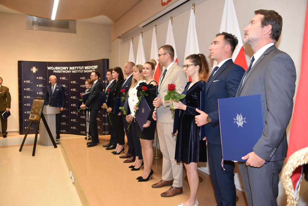 Rozpoczęcie roku akademickiego w wojskowym instytucie medycznym. Ceremonia rozdania dyplomów w auli. Studenci stoją na podeście przy ścianie, za nimi rozwieszone flagi Polski.