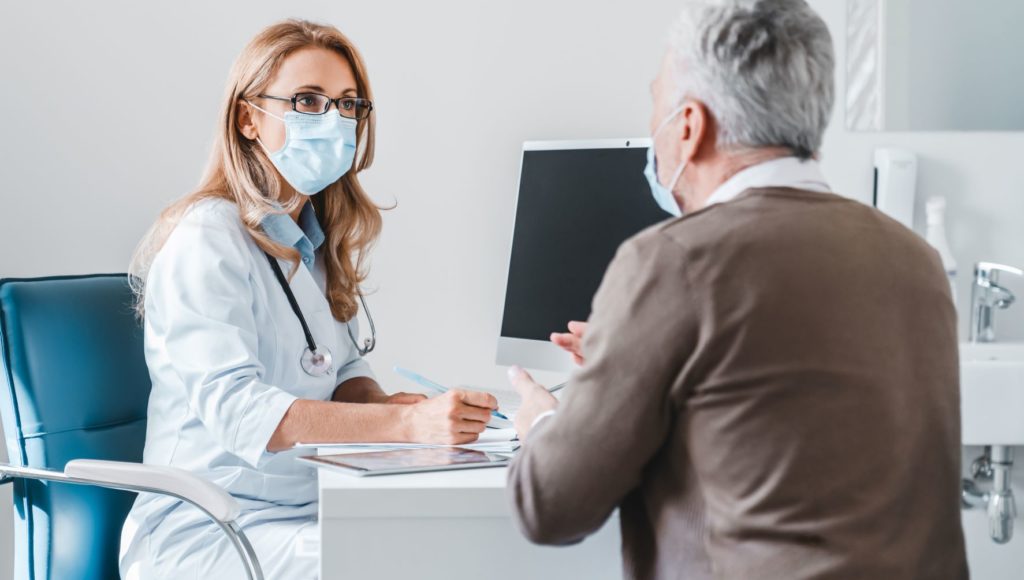 Pacjent rozmawia z panią doktor w gabinecie lekarskim, obaj mają założone maseczki na nos oraz usta.