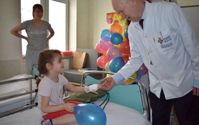 Prof Kalicki z małą pacjentką siedząca na łóżku szpitalnym.