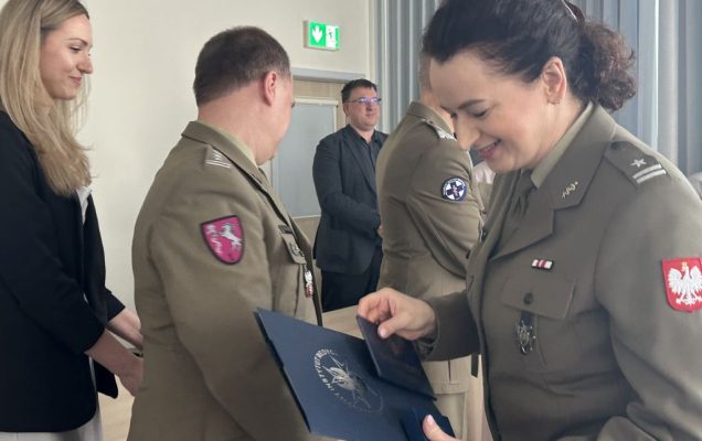 Studentka ubrana w wojskowy trzyma dyplom.