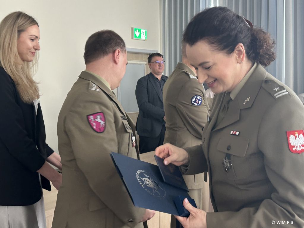 Studentka ubrana w wojskowy trzyma dyplom.