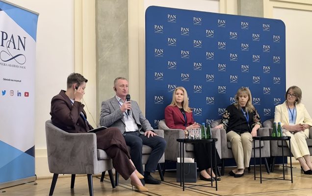 Panel dyskusyjny konferencji, siedzący prelegenci z animi tablica z logotypami PAN.