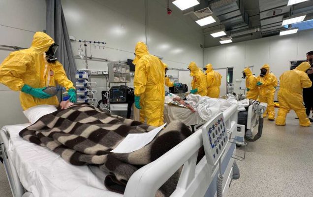 Medycy w żółtych kombinezonach i maskach przeciwgazowych podczas kursy CBRN w żółtych kombinezonach na sali szpitalnej.