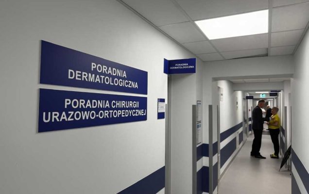 Korytarz poradni. Na ścianie wiszą tablice Poradni dermatologicznej i Poradni Chirurgii Urazowo Ortopedycznej.