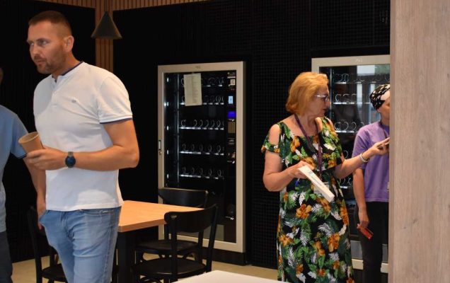 W pomieszczeniu przy automatach pracownicy i pacjenci korzystający z automatów z przekąskami.