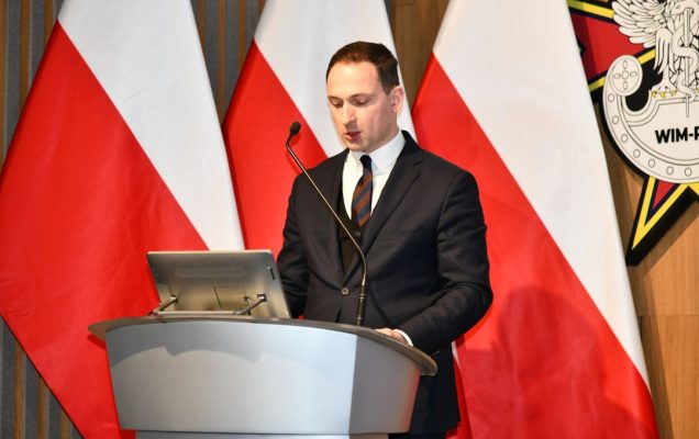 Jan Gębalski przy mównicy z tyłu flagi RP.