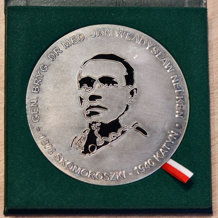 Srebrny medal w aksamitnym zielonym pudełku. Medal przedstawia twarz mężczyzny.