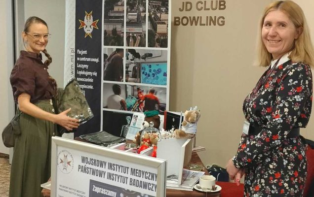 Dwie uśmiechnięte pracowniczki Wydziału Kształcenia Podyplomowego Lekarzy (CKP) stoją przy stoisku WIM-PIB.
