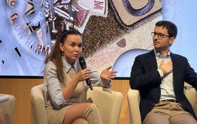 Prelegent i prelegentka siedzący w fotelach podczas panelu dyskusyjnego. Kobieta mówi do mikrofonu. Za ich plecami na dużym wyświetlaczu fragment prezentacji.