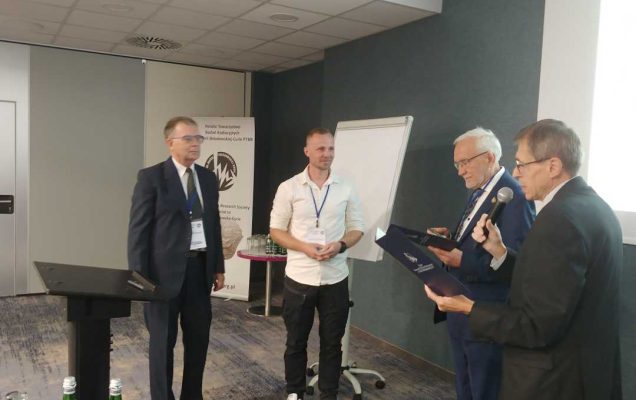 Sala konferencyjna. Prowadzący wydarzenie i laureaci chwilę przed wręczeniem nagrody.
