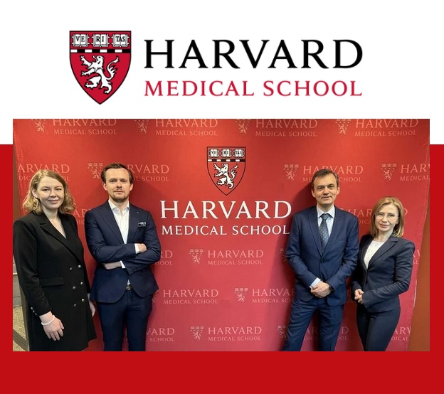 Laureaci studiów pozują na tle ścianki z logo Harvardu.