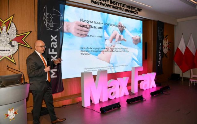 Prelegent podczas konferencji, obok stojący napis Max Fax i ekran ze slajdem z konferencji.