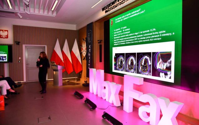 Prelegentka prowadząca wykład. Za nią logo WIM. Obok stoi różowa dekoracja z napisem Max Fax i ekran z wyświetlonym slajdem z konferencji.