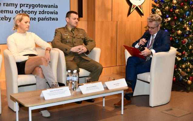 Siedzący w fotelach paneliści podczas sesji, za nimi fragment wyświetlanej prezentacji.