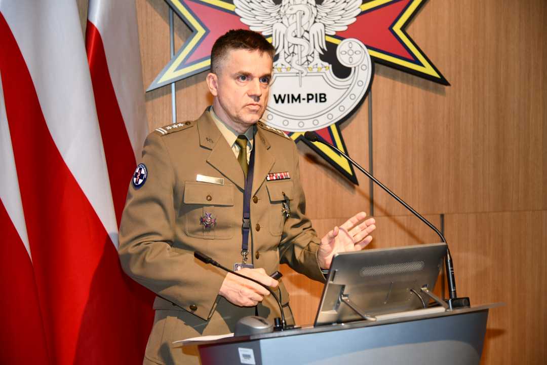 Jarosław Kowal przy mównicy podczas wykładu . Za nim logo WIM.