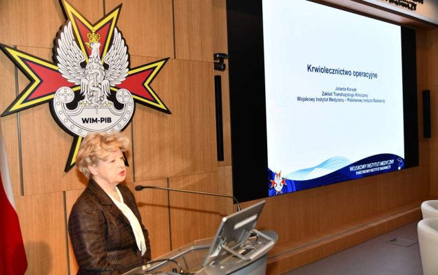 dr hab. n. med. Jolanta Korsak, kierownik Zakładu Transfuzjologii Klinicznej WIM-PIB przy mównicy za jej plecami na ekranie slajd z konferencji.