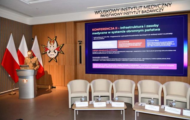 Grzegorz Gielerak przy mównicy, obok niego na ekranie wyświetlony slajd z konferencji.