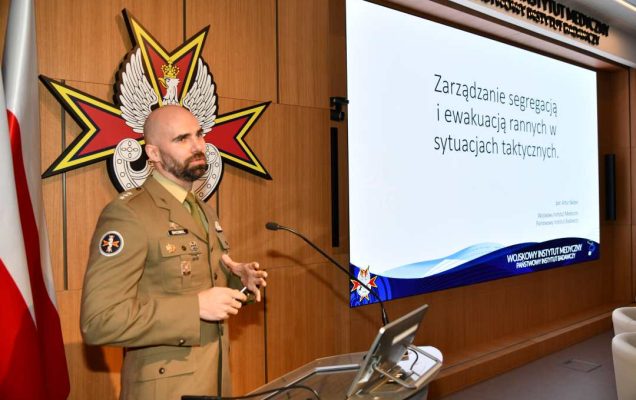 por. mgr Artur Skobel przy mównicy. Za jego plecami na ekranie slajd z konferencji.