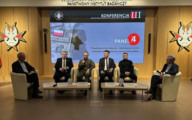 Paneliści siedzący w fotelach. Za nimi ogromny ekran z planszą konferencji.