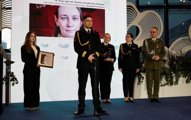 Członkowie Akademii Pożarniczej na scenie. Za nimi na ekranie zdjęcie Kariny Jarosławskiej-Kolman.