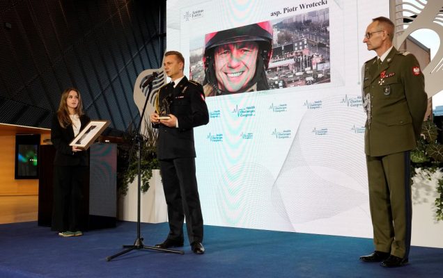 Piotr Wrotecki przy mikrofonie za nimna ekranie plansza z jego zdjęciem.