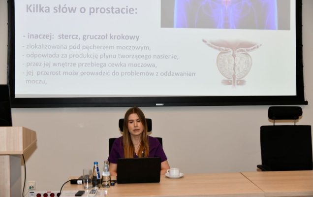 Agnieszka Grabińska za biurkiem podczas wykładu, za nią na ekranie slajd z prezentacji.