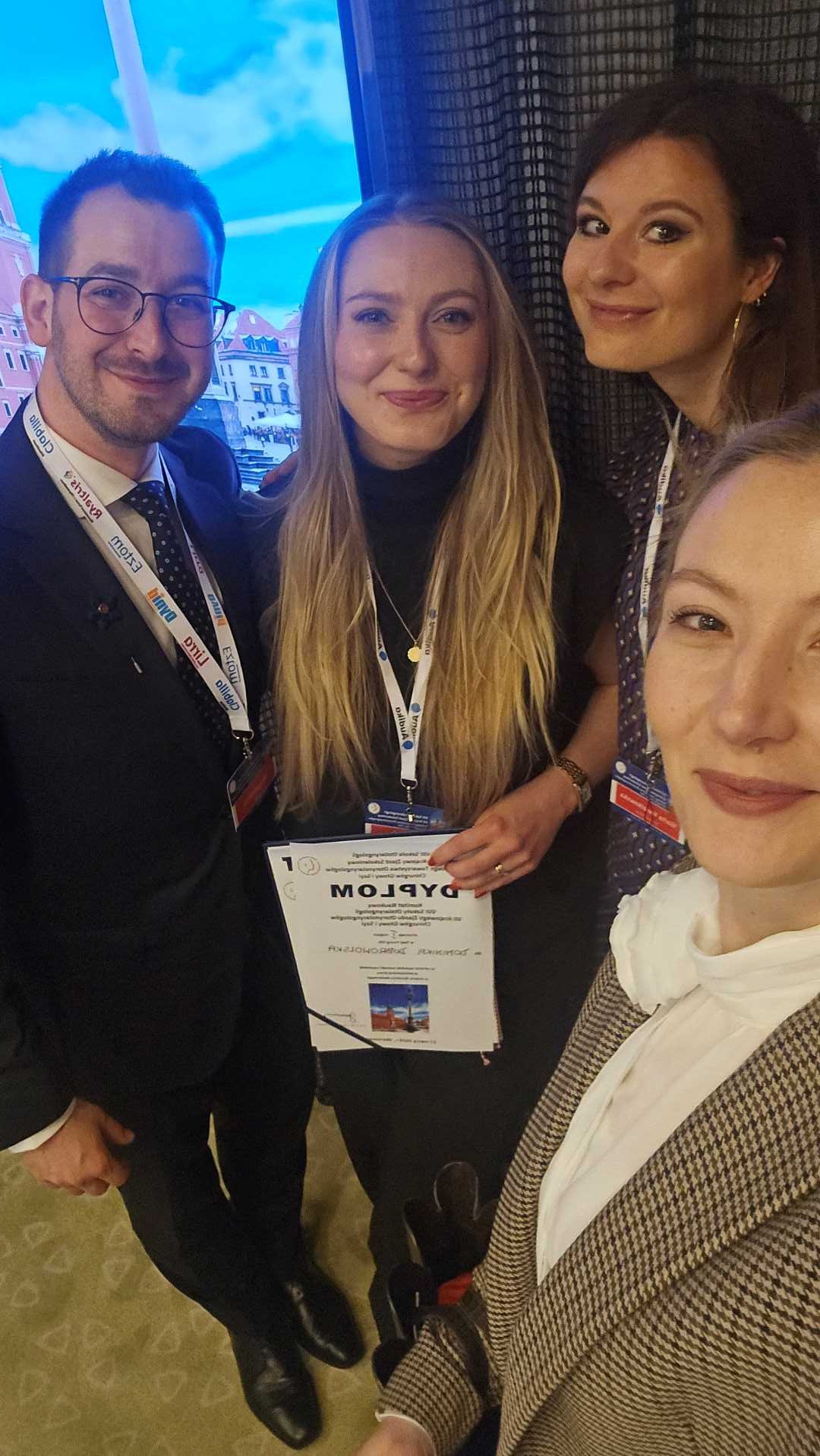 Selfie prelegentów. Trzy młode kobiety i młody mężczyzna, za nimi wyświetlacz z prezentacją.