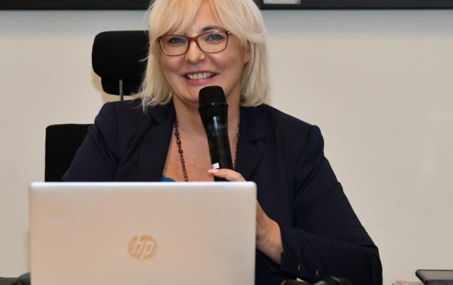 Katarzyna Łukowska uśmiechnięta z mikrofonem przed laptopem