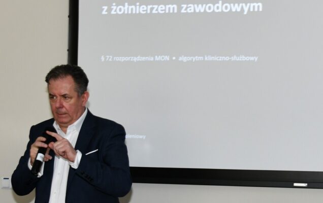 Radosław Tworus z mikrofonem, za nim slajd prezentacji.