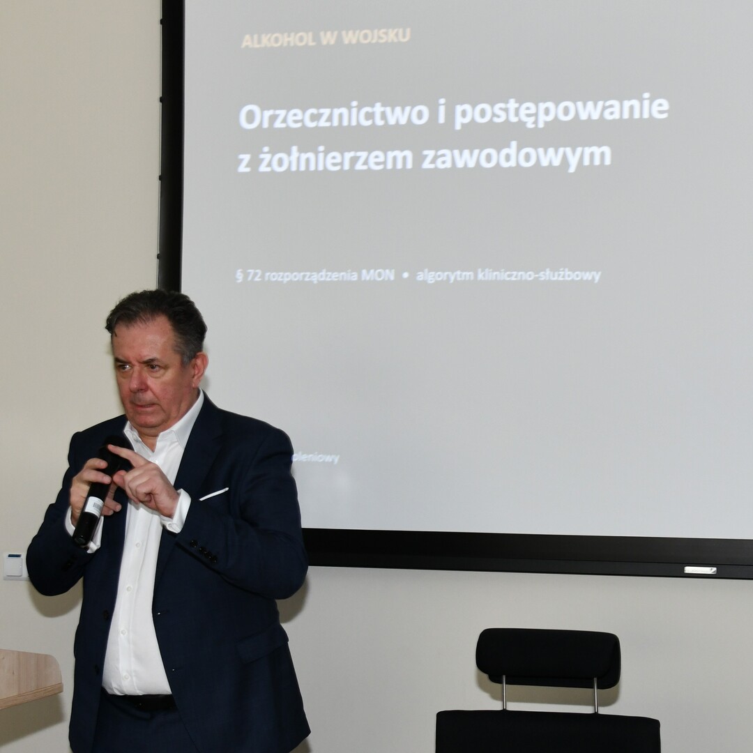 Radosław Tworus z mikrofonem, za nim slajd prezentacji.