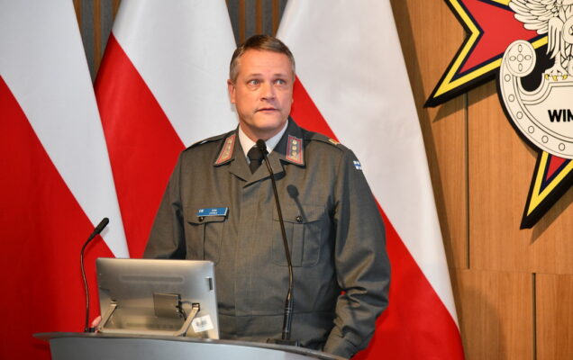 Gość Konferencji Tero Levola przy mównicy, za nim trzy flagi polski, oraz logo WIMu