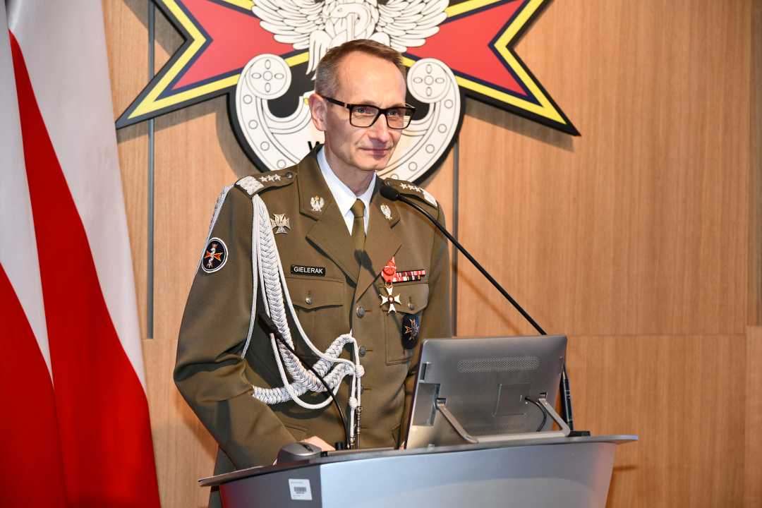 Grzegorz Gielerak przy mównicy. Za jego plecami flaga Polski i logotyp WIM-PIB.